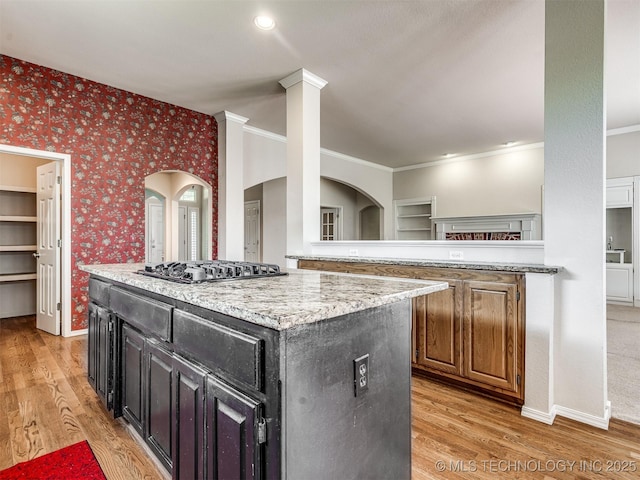 kitchen with dark cabinets, wallpapered walls, a center island, light wood-style floors, and stainless steel gas stovetop
