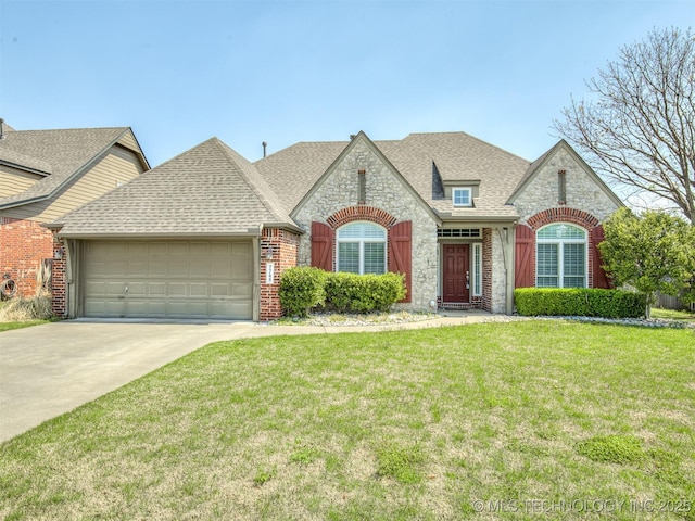 french provincial home with roof with shingles, a front yard, stone siding, a garage, and driveway