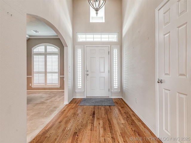 entryway featuring arched walkways, a high ceiling, baseboards, and carpet