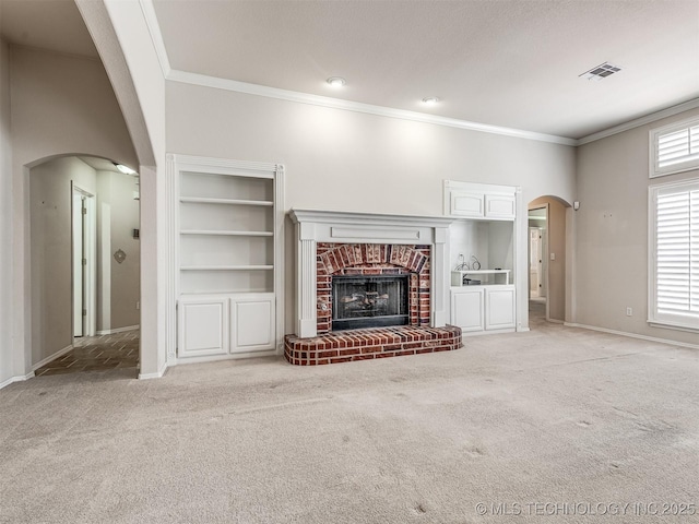unfurnished living room with visible vents, arched walkways, a brick fireplace, crown molding, and light carpet