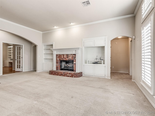 unfurnished living room with crown molding, arched walkways, light colored carpet, visible vents, and a brick fireplace