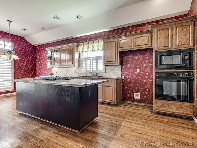 kitchen with light wood-type flooring, black appliances, a kitchen island, lofted ceiling, and wallpapered walls