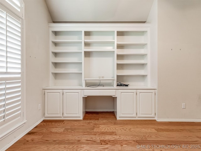 unfurnished office with built in study area, light wood-style floors, and baseboards