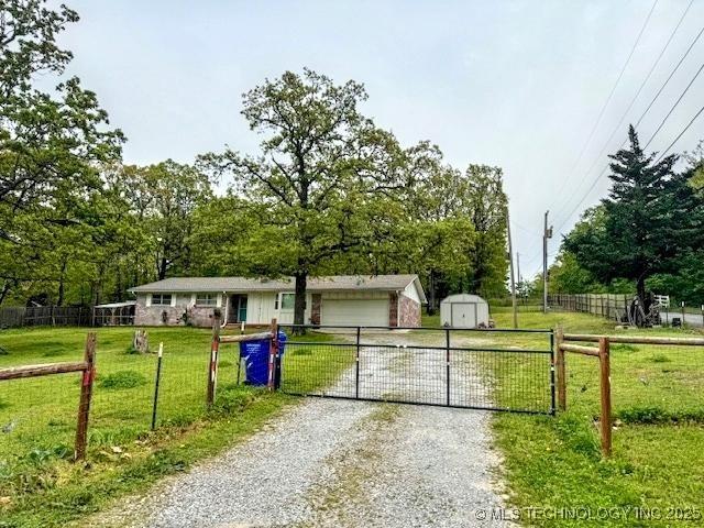 view of front of house featuring fence, an attached garage, gravel driveway, a shed, and a front yard