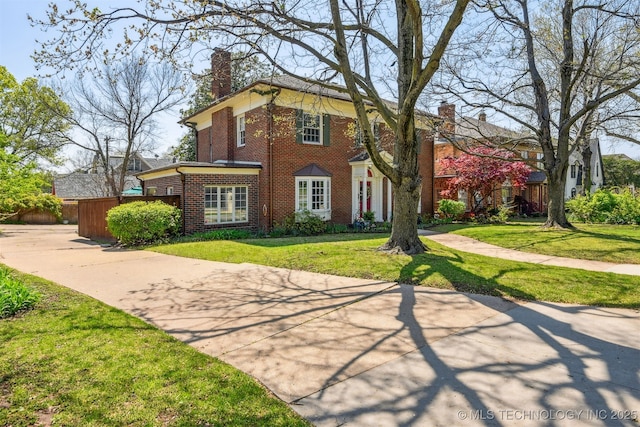 view of front of home featuring brick siding, a chimney, and a front lawn