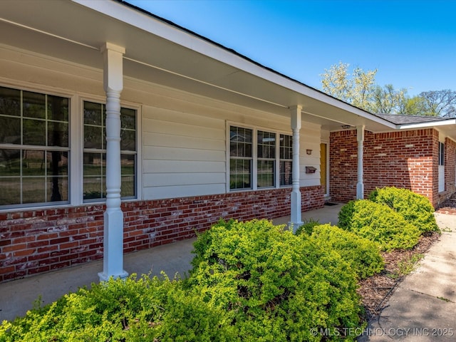 view of exterior entry featuring brick siding and covered porch