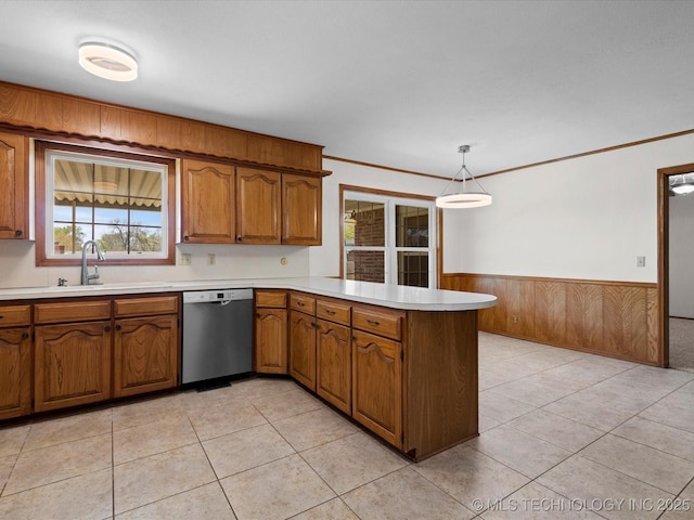 kitchen featuring stainless steel dishwasher, a peninsula, a sink, wainscoting, and brown cabinets