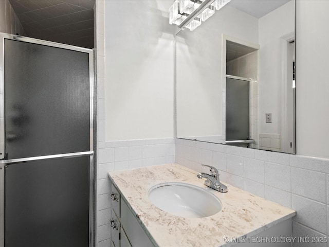 full bath featuring tile walls, a shower stall, vanity, and a wainscoted wall