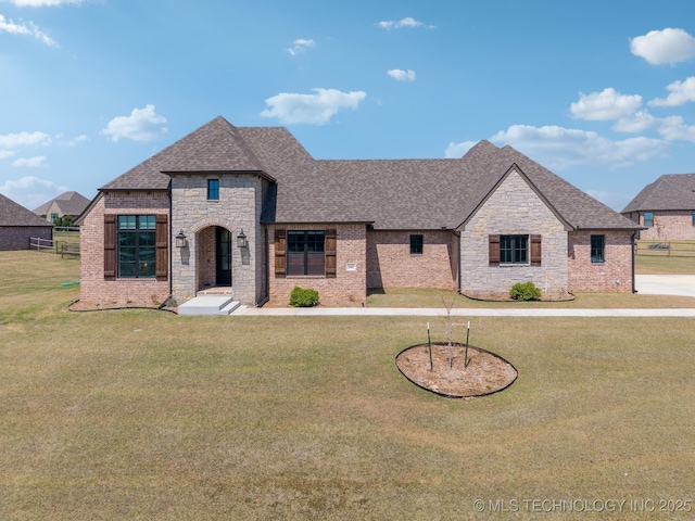 french country inspired facade featuring a front yard, roof with shingles, and stone siding