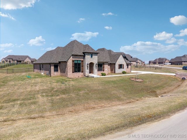 french country home with brick siding, stone siding, fence, and a front lawn