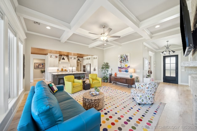 living area featuring light wood-type flooring, a fireplace, beam ceiling, ceiling fan with notable chandelier, and coffered ceiling