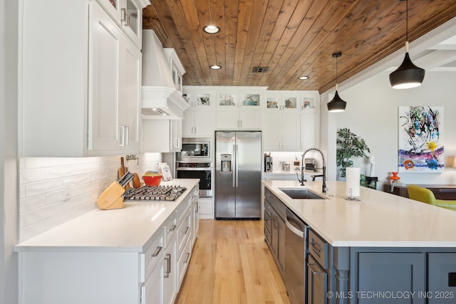 kitchen with wooden ceiling, a sink, white cabinetry, stainless steel appliances, and custom range hood