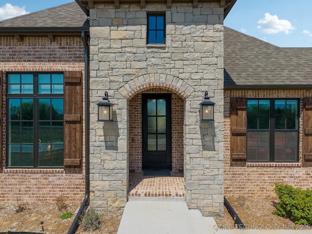 doorway to property featuring brick siding, a shingled roof, and stone siding
