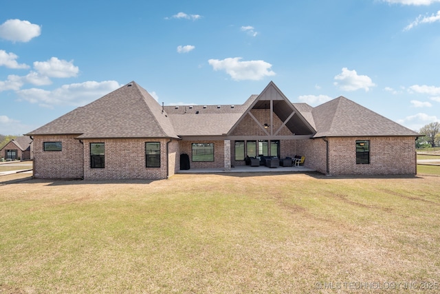 back of property with a yard, a shingled roof, brick siding, and a patio