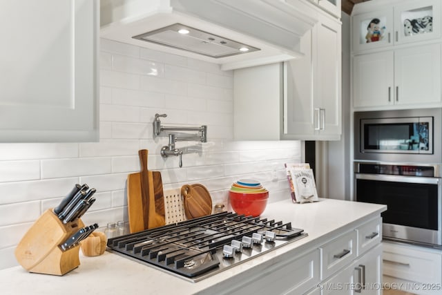 kitchen with tasteful backsplash, glass insert cabinets, white cabinets, and stainless steel appliances