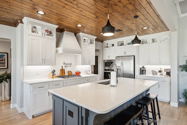 kitchen featuring a sink, light countertops, premium range hood, a kitchen island with sink, and stainless steel appliances