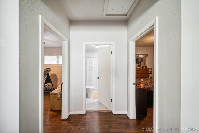 hallway featuring dark wood-type flooring, baseboards, and attic access
