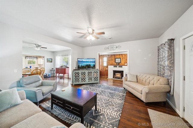 living area featuring baseboards, a brick fireplace, visible vents, ceiling fan, and wood finished floors