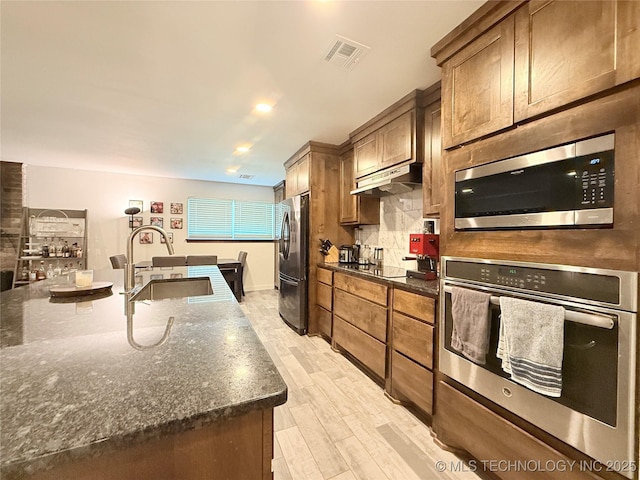 kitchen featuring appliances with stainless steel finishes, under cabinet range hood, visible vents, decorative backsplash, and a sink