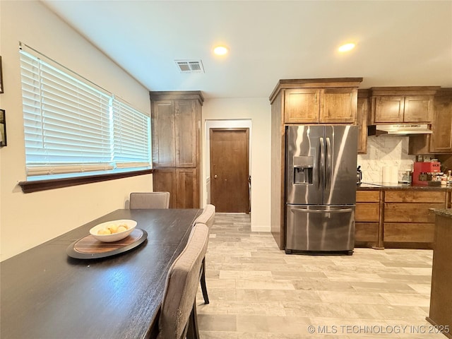 interior space with brown cabinetry, visible vents, stainless steel refrigerator with ice dispenser, under cabinet range hood, and backsplash