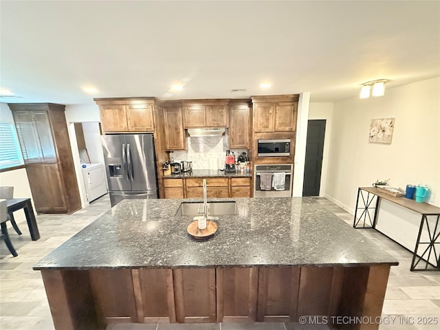 kitchen featuring appliances with stainless steel finishes, a large island, under cabinet range hood, decorative backsplash, and a sink