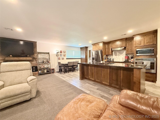 kitchen featuring open floor plan, dark countertops, under cabinet range hood, stainless steel appliances, and a sink