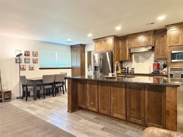 kitchen featuring backsplash, under cabinet range hood, visible vents, appliances with stainless steel finishes, and a sink