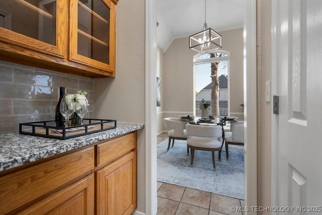 interior space featuring tasteful backsplash, glass insert cabinets, an inviting chandelier, and brown cabinets