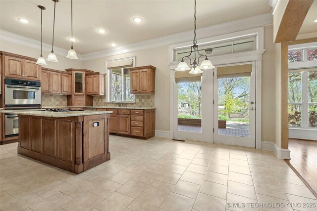 7505 S 4th St, Broken Arrow, OK 74011 - kitchen featuring brown cabinets, backsplash, a chandelier, a kitchen island, and crown molding