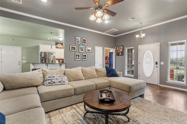 living area with ornamental molding, visible vents, wood finished floors, and ceiling fan with notable chandelier