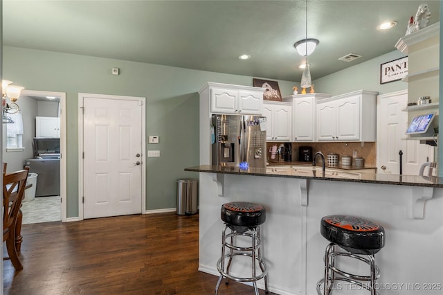 kitchen featuring dark stone counters, stainless steel fridge with ice dispenser, washer / clothes dryer, white cabinets, and a breakfast bar area