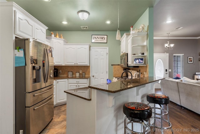 kitchen featuring dark stone countertops, appliances with stainless steel finishes, a peninsula, white cabinetry, and a breakfast bar area