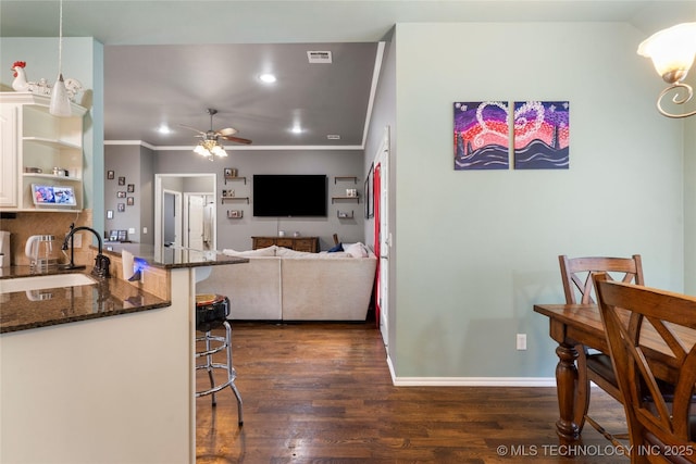 kitchen featuring a ceiling fan, visible vents, a breakfast bar, a sink, and dark wood-style floors
