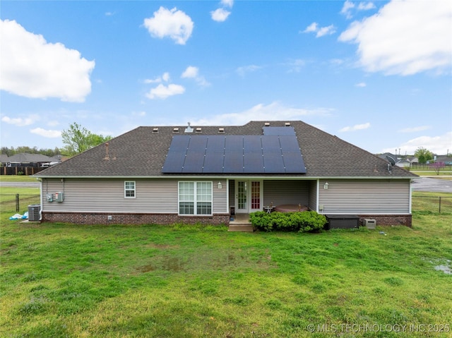 rear view of house with roof with shingles, fence, a lawn, and roof mounted solar panels