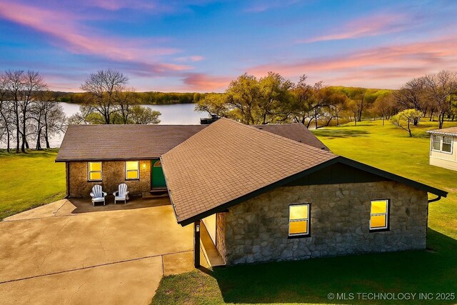 view of front of house featuring a front yard, driveway, stone siding, and a shingled roof