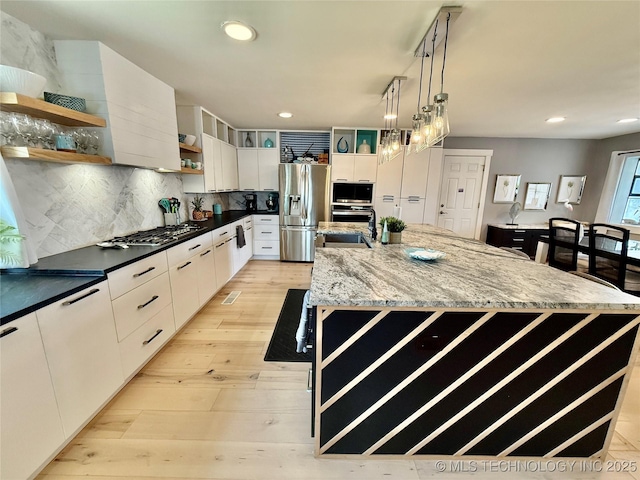 kitchen with light wood-style floors, an island with sink, open shelves, stainless steel appliances, and backsplash