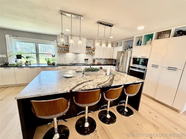 kitchen with tasteful backsplash, open shelves, appliances with stainless steel finishes, white cabinetry, and a breakfast bar area