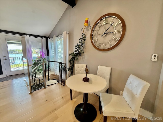 dining area with light wood-style flooring and vaulted ceiling with beams