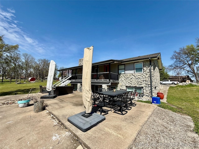 rear view of property with a patio area, stone siding, a lawn, outdoor dining space, and stairway