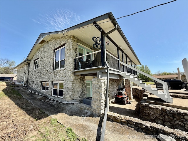 view of home's exterior featuring stairs, a balcony, and stone siding