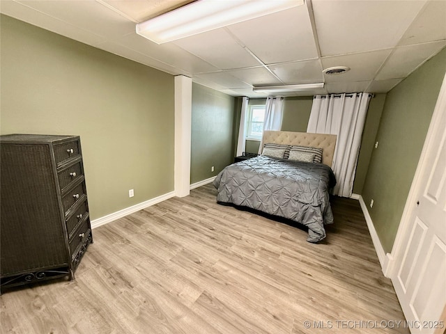 bedroom with light wood finished floors, baseboards, a drop ceiling, and visible vents