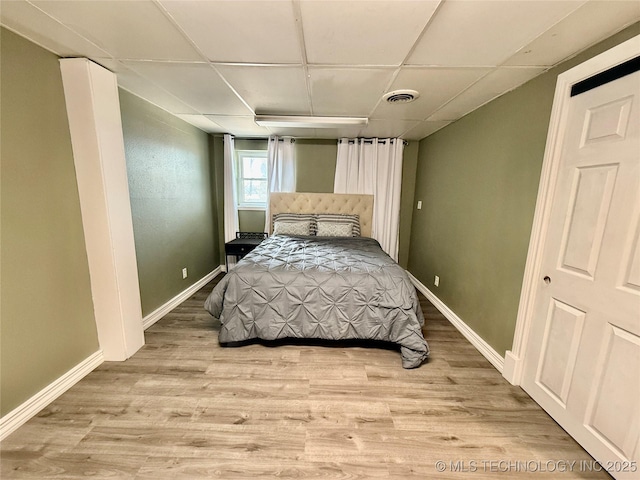 bedroom with light wood-style floors, visible vents, a drop ceiling, and baseboards