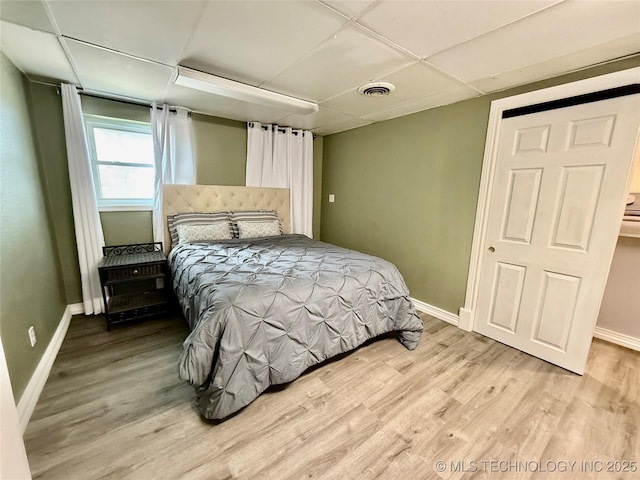 bedroom featuring light wood-style floors, baseboards, a drop ceiling, and visible vents