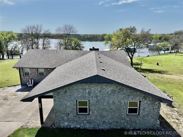 view of property exterior featuring a yard, a shingled roof, stone siding, and a water view