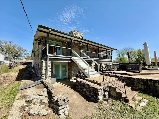 rear view of house with a patio, a chimney, stairway, french doors, and stone siding