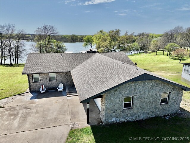 view of side of home with roof with shingles, stone siding, a water view, and a lawn