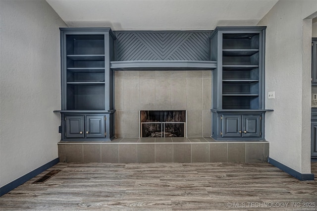 804 S Sooner Rd, Midwest City, OK 73110 - unfurnished living room with visible vents, wood finished floors, a tile fireplace, baseboards, and built in shelves