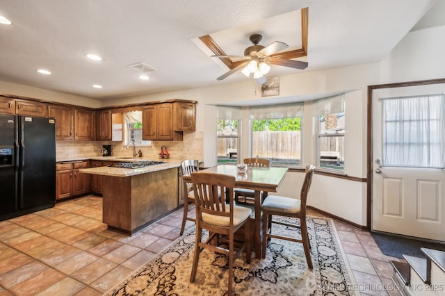 1604 S Chestnut Ave, Broken Arrow, OK 74012 - kitchen with black fridge, tasteful backsplash, a peninsula, brown cabinetry, and light stone counters