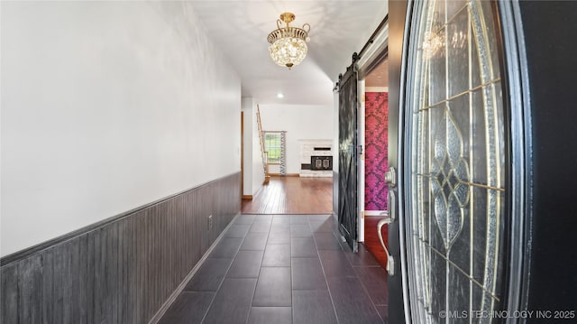 hallway featuring a barn door, dark wood-style floors, an inviting chandelier, and a wainscoted wall