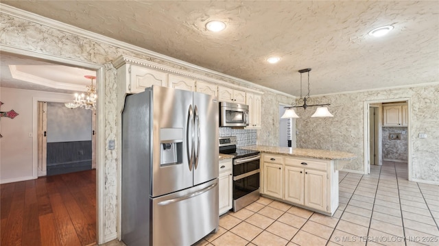 kitchen featuring a peninsula, a textured ceiling, ornamental molding, a chandelier, and appliances with stainless steel finishes